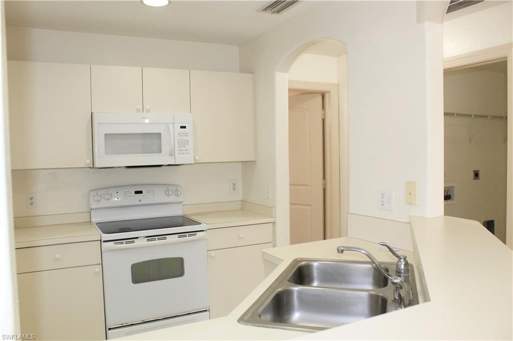 Kitchen featuring white appliances, light countertops, white cabinetry, and arched walkways