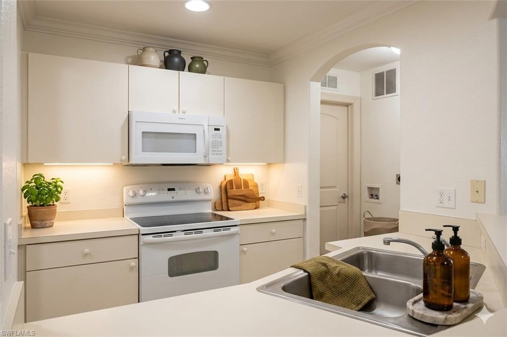 Virtual staged Kitchen with white appliances, ornamental molding, light countertops, white cabinets, and arched walkways