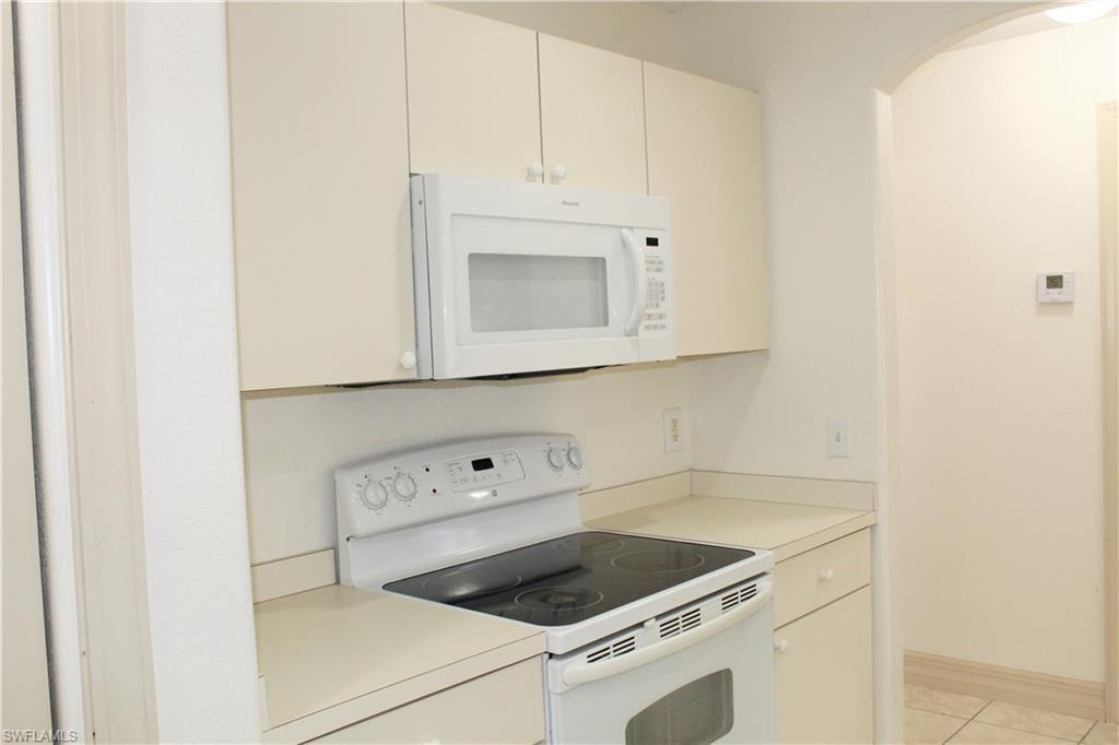 Kitchen with white appliances, light countertops, arched walkways, light tile patterned floors, and cream cabinetry