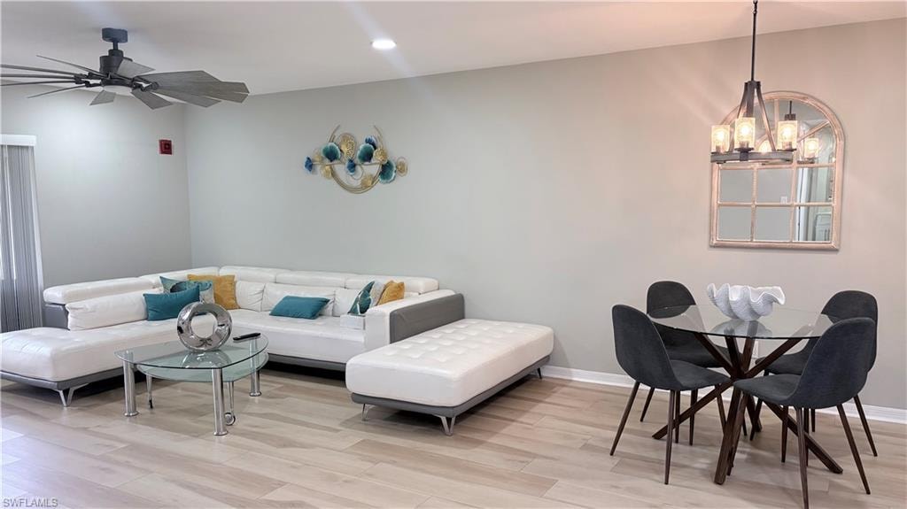 Living area with light wood-style floors, ceiling fan, and hanging lights
