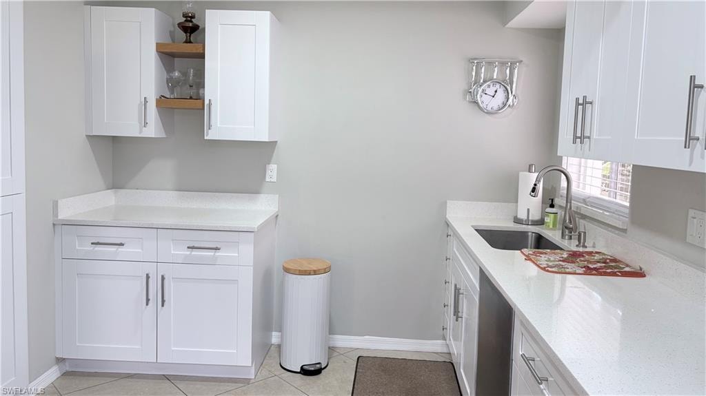 Kitchen with white cabinetry, light stone counters, open shelves, light tile patterned floors, and stainless steel dishwasher