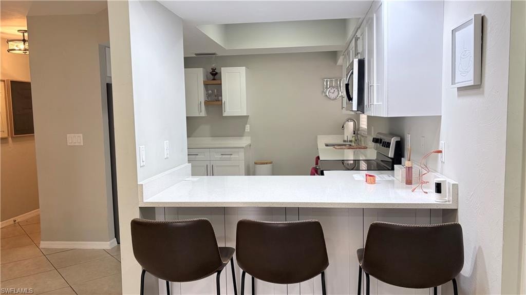 Kitchen featuring white cabinets, electric range oven, a peninsula, a kitchen breakfast bar, and stainless steel microwave