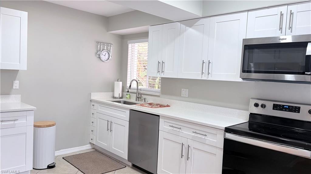 Kitchen featuring stainless steel appliances, white cabinetry, light stone countertops, and light tile patterned floors