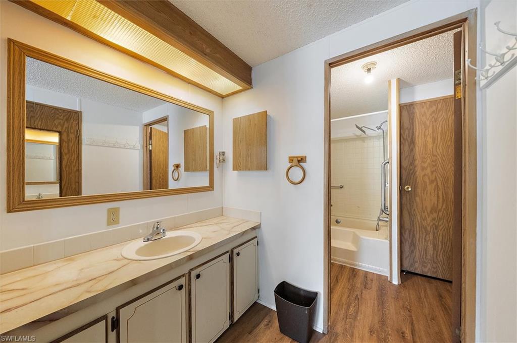 Full bathroom featuring a textured ceiling, vanity, shower / tub combination, and dark wood-type flooring