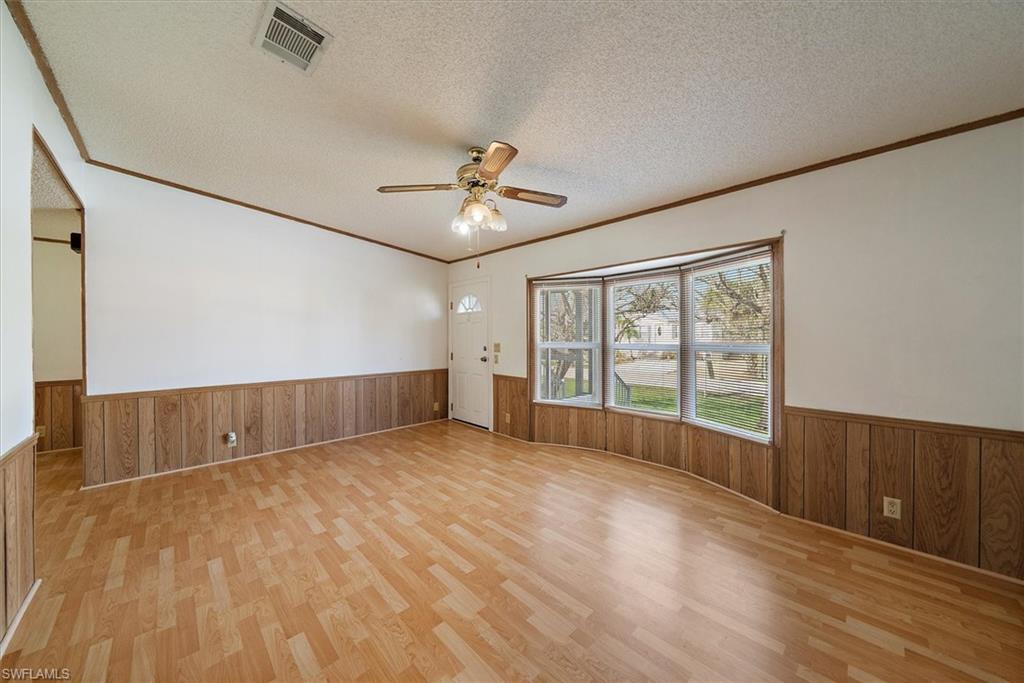Empty room featuring wooden walls, a textured ceiling, wainscoting, ornamental molding, and a ceiling fan