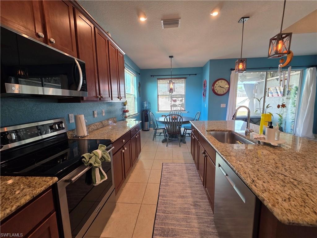 Kitchen with stainless steel appliances, light stone countertops, hanging light fixtures, light tile patterned floors, and a textured ceiling