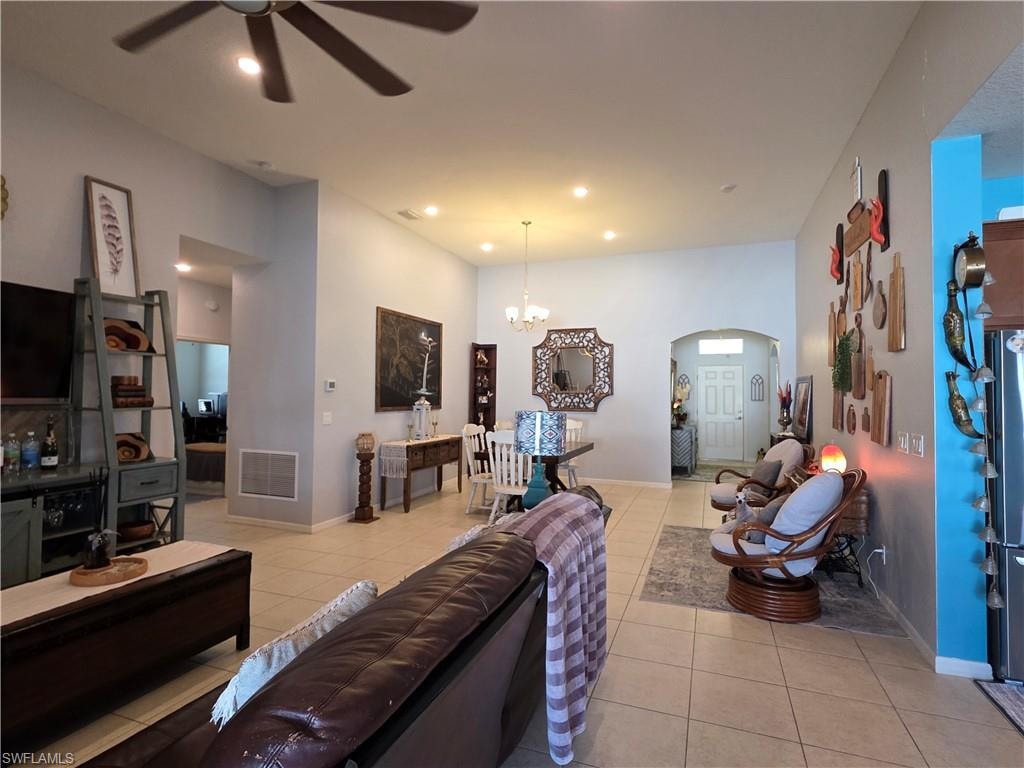 Living area with a ceiling fan, light tile patterned floors, suspended lighting, arched walkways, and a high ceiling