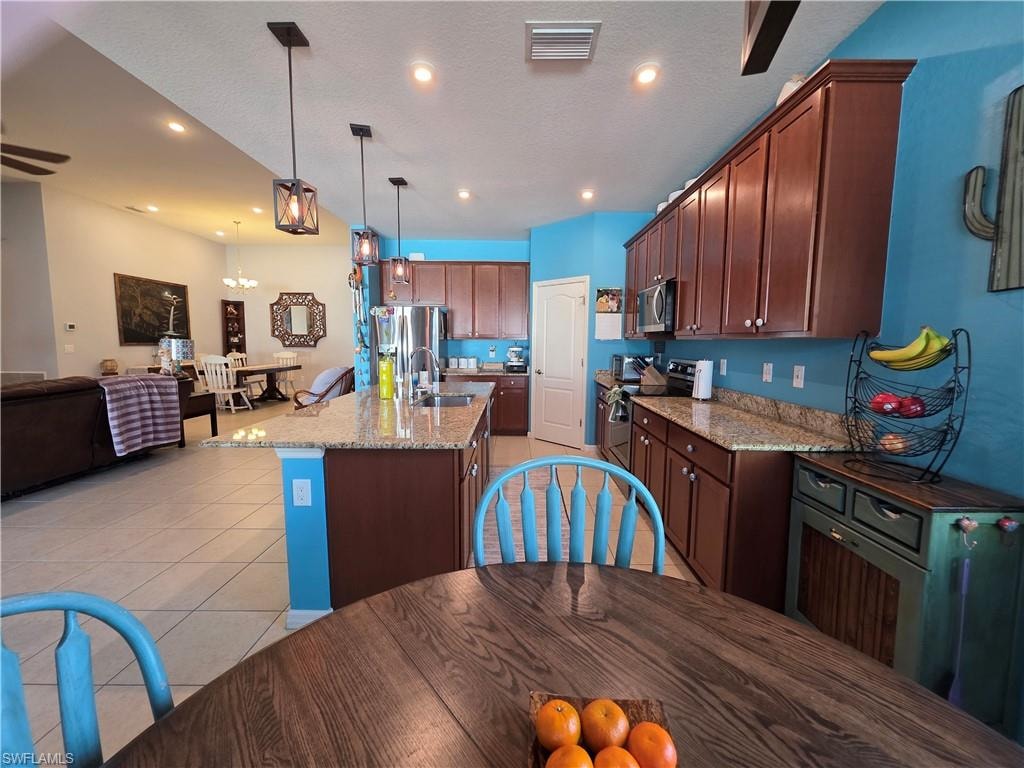Kitchen with light stone countertops, open floor plan, stainless steel appliances, a center island with sink, and light tile patterned flooring