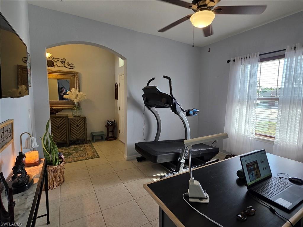 Workout area featuring a ceiling fan, arched walkways, and light tile patterned floors
