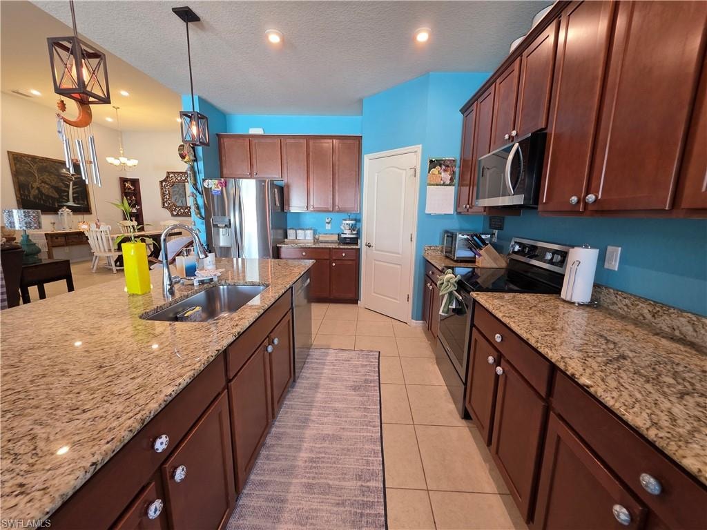 Kitchen with stainless steel appliances, a textured ceiling, light stone countertops, light tile patterned floors, and pendant lighting