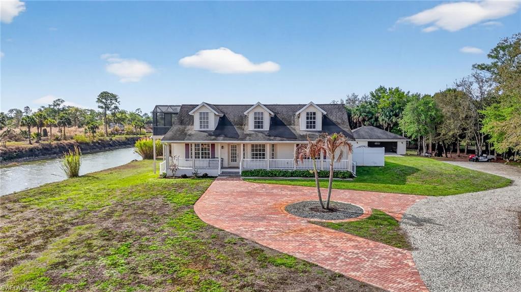 Cape cod-style house with covered porch, a front yard, curved driveway, and a water view