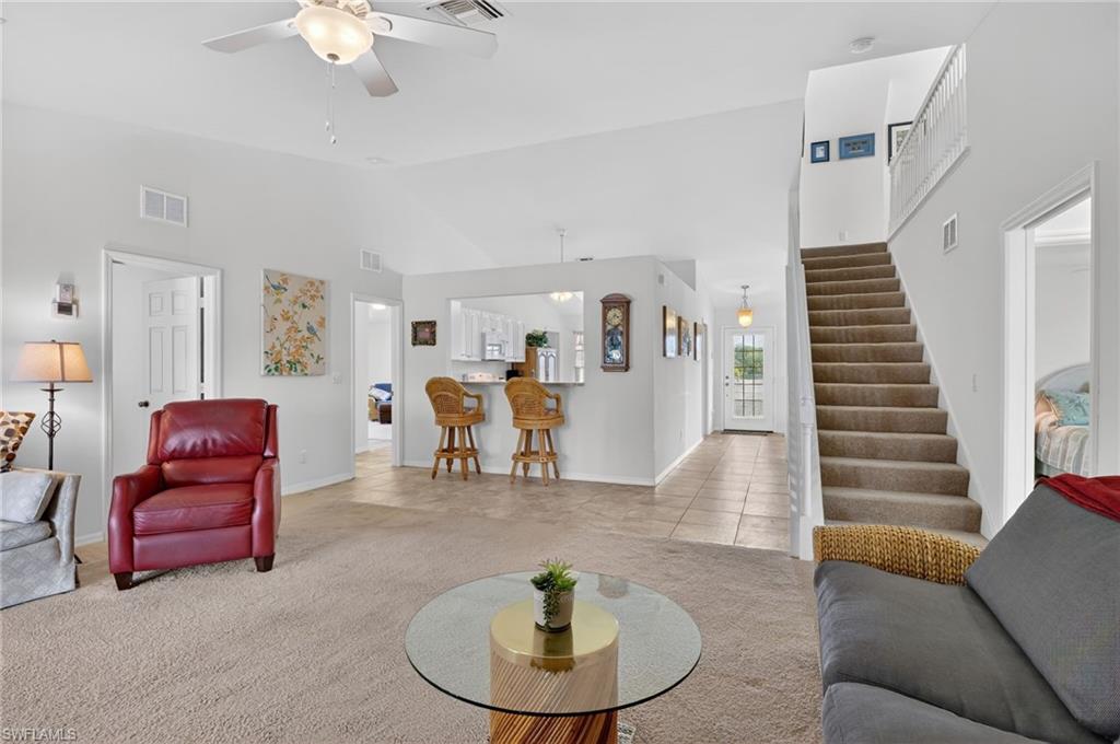 Living area featuring light carpet, light tile patterned flooring, vaulted ceiling, and a ceiling fan