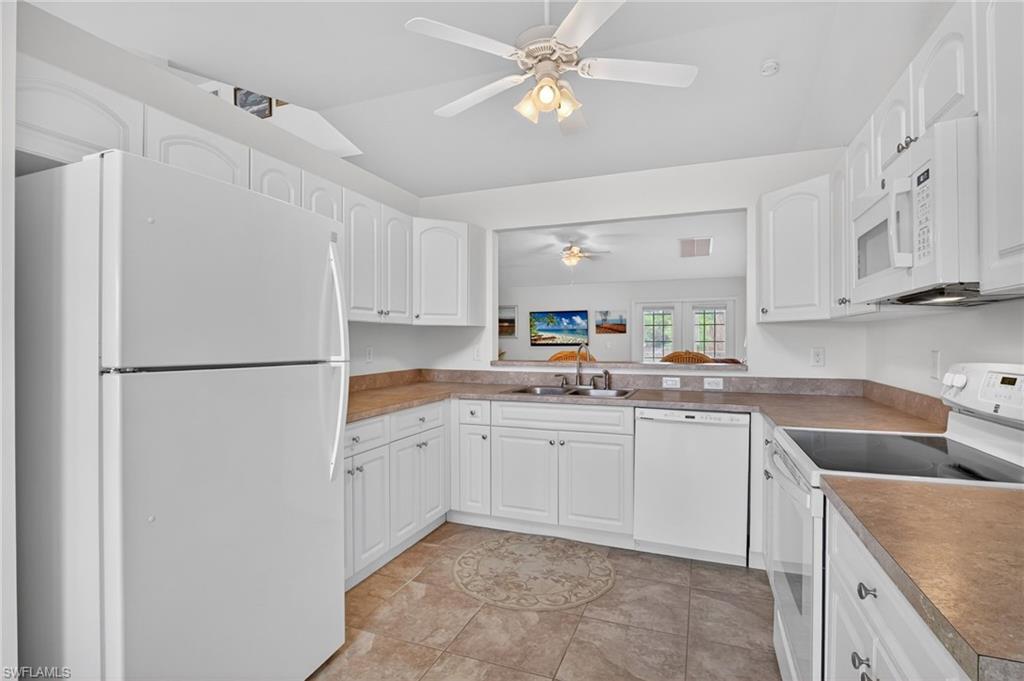 Kitchen with white appliances, white cabinetry, light tile patterned floors, vaulted ceiling, and a ceiling fan