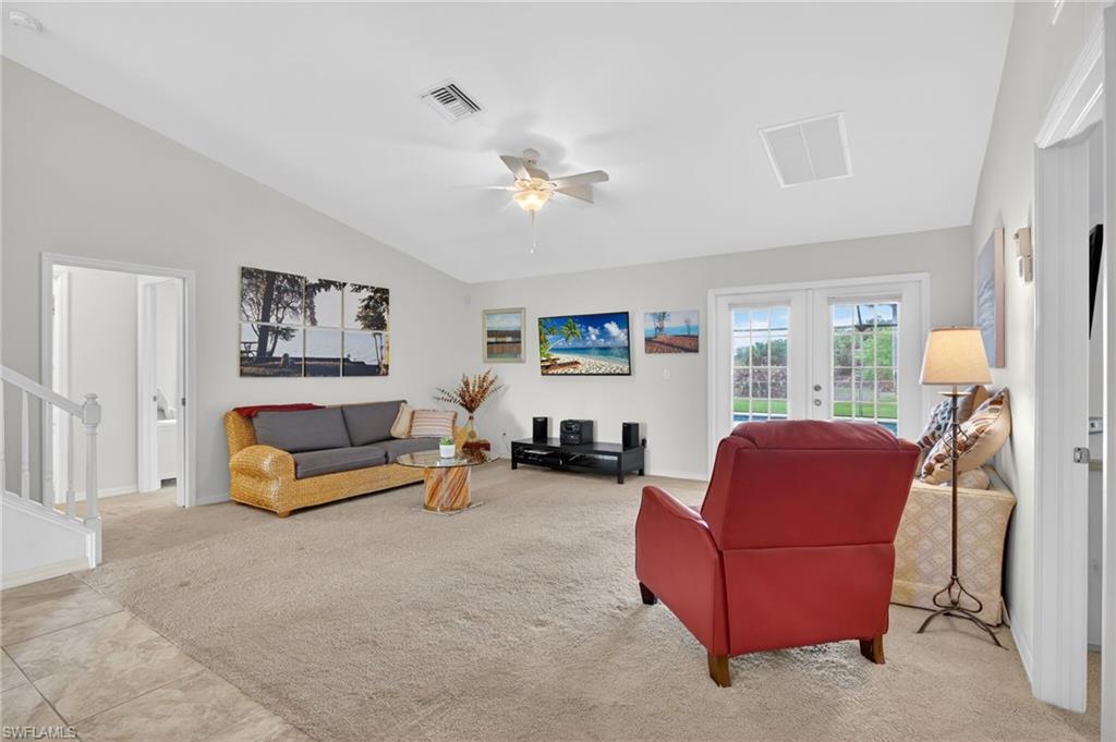 Living room featuring ceiling fan, light carpet, french doors, and vaulted ceiling