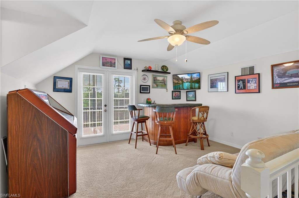 Indoor dry bar with a ceiling fan, dark countertops, light carpet, and lofted ceiling
