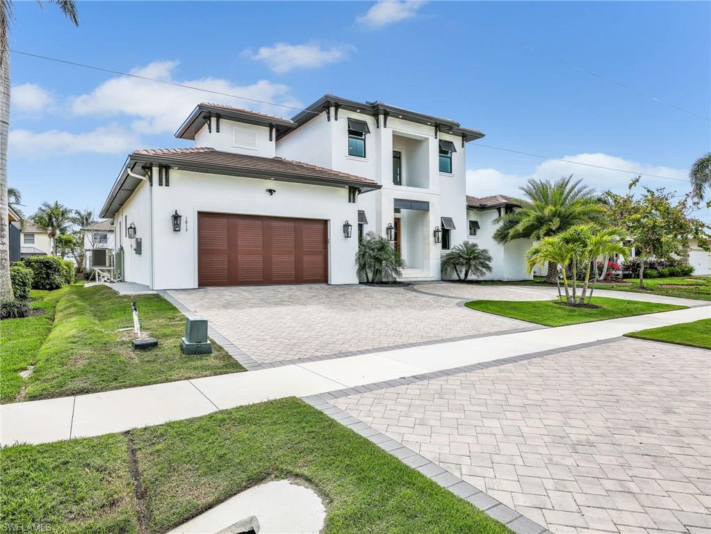 View of front of property with decorative driveway, stucco siding, a garage, a front lawn, and a tiled roof