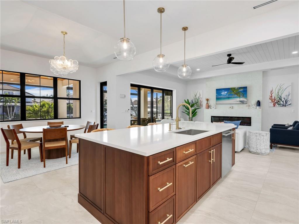 Kitchen featuring open floor plan, an island with sink, a fireplace, hanging lights, and wood finish cabinets