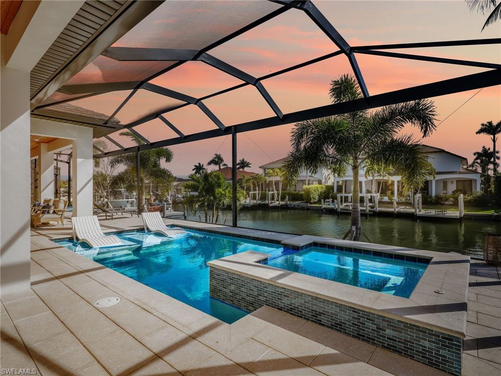 Pool at dusk with a patio, a water view, a pool with connected hot tub, glass enclosure, and a sunroom