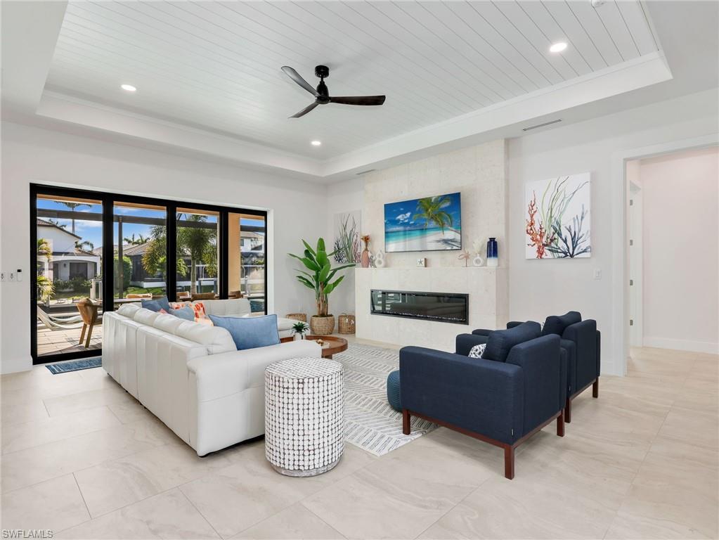 Living room with ceiling fan, a fireplace, a wood tray ceiling, and recessed lighting