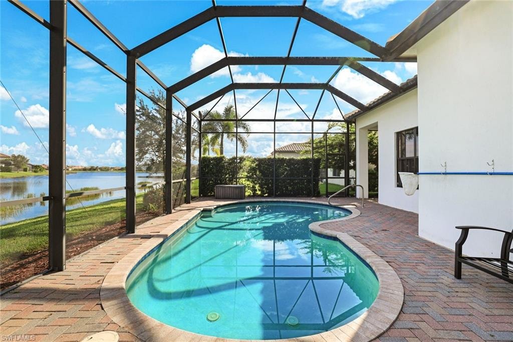 Outdoor pool with a patio area, a water view, glass enclosure, and a sunroom