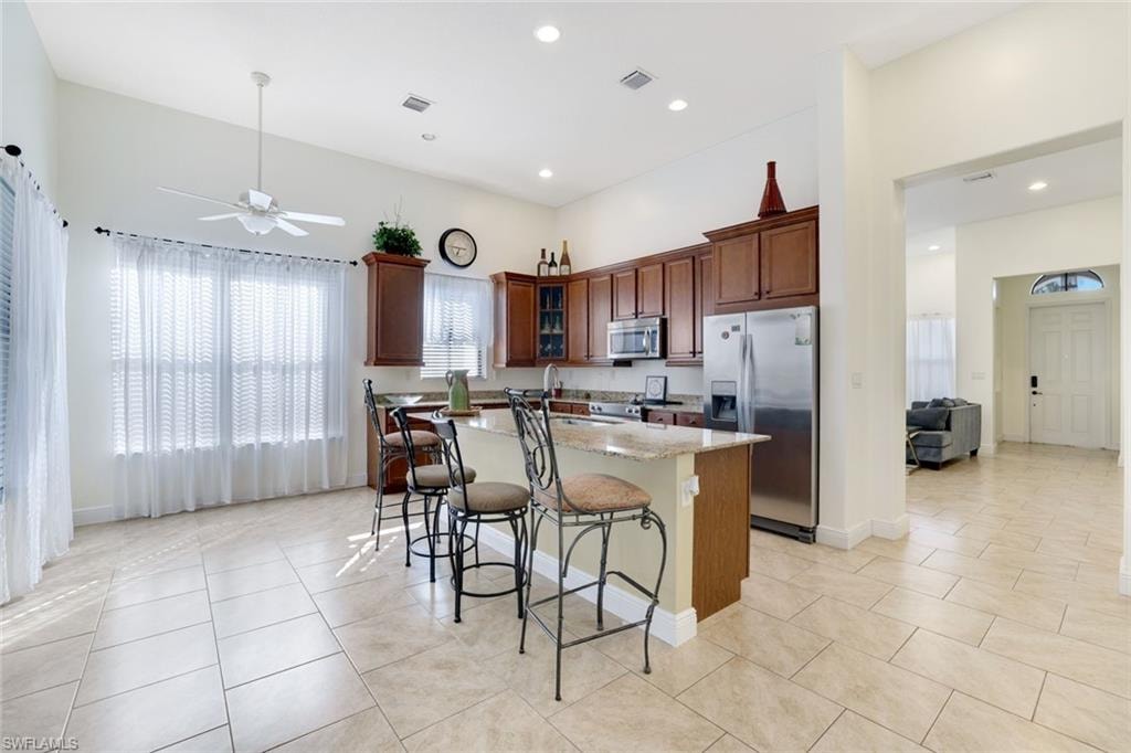 Kitchen with appliances with stainless steel finishes, light stone countertops, a breakfast bar area, glass insert cabinets, and a kitchen island with sink
