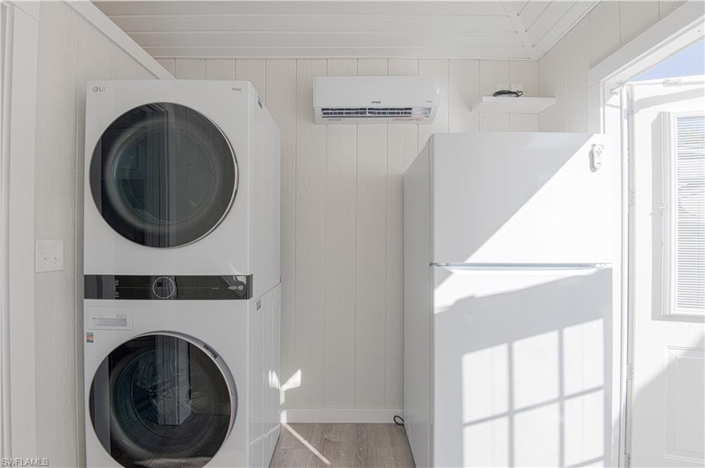 Laundry room with stacked washer and dryer, wood walls, and light wood-style floors