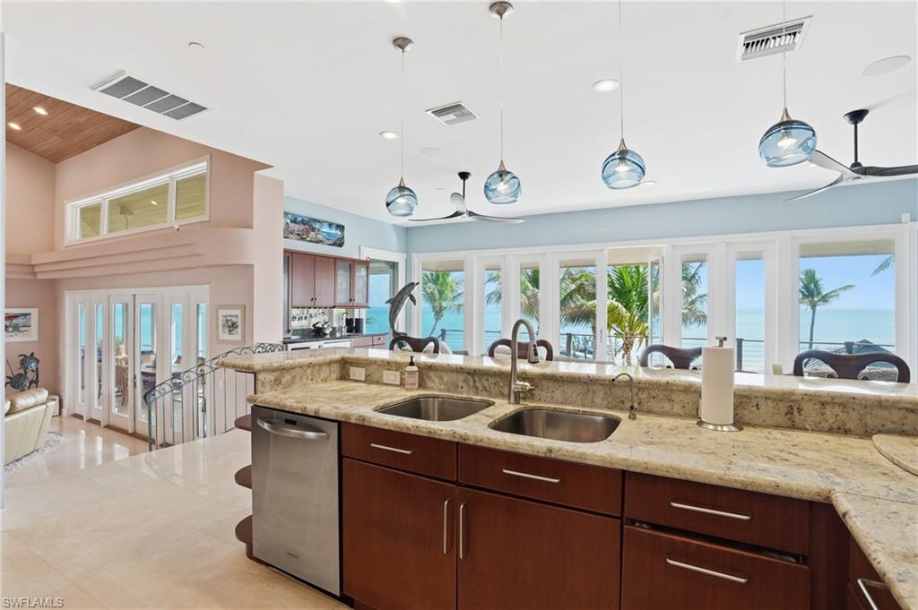 Kitchen with open floor plan, stainless steel dishwasher, light stone counters, hanging light fixtures, and dark wood finish cabinets