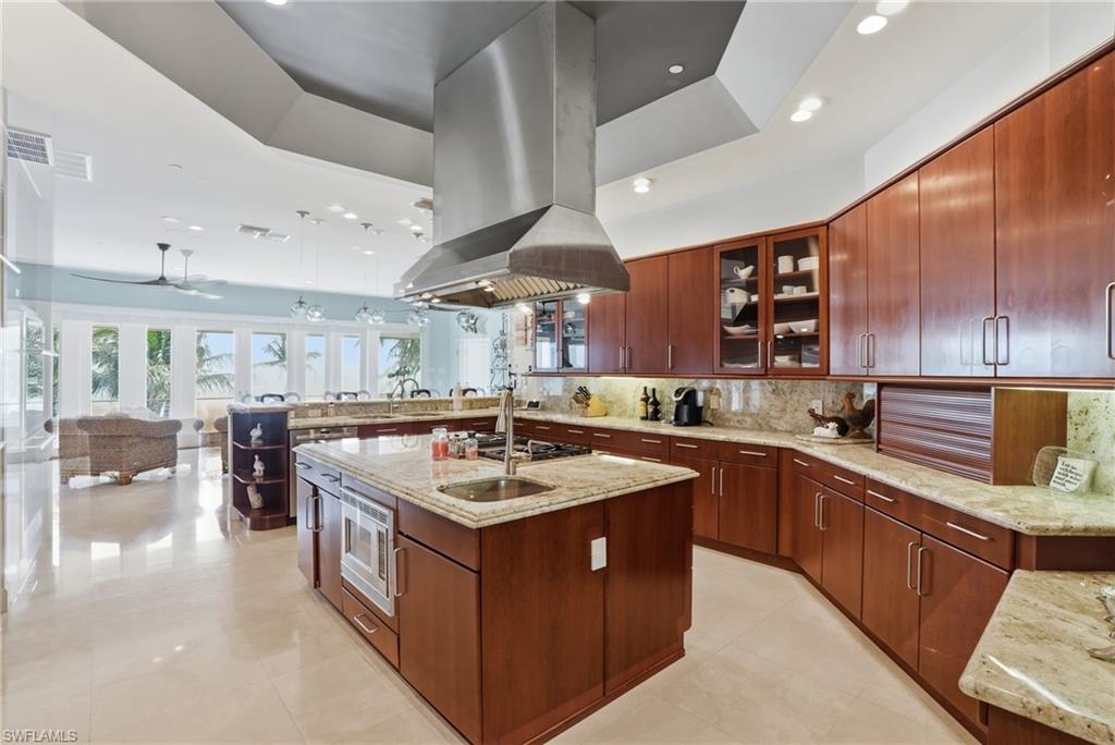 Kitchen with glass fronted cabinets, light stone counters, open floor plan, a peninsula, and an island with sink