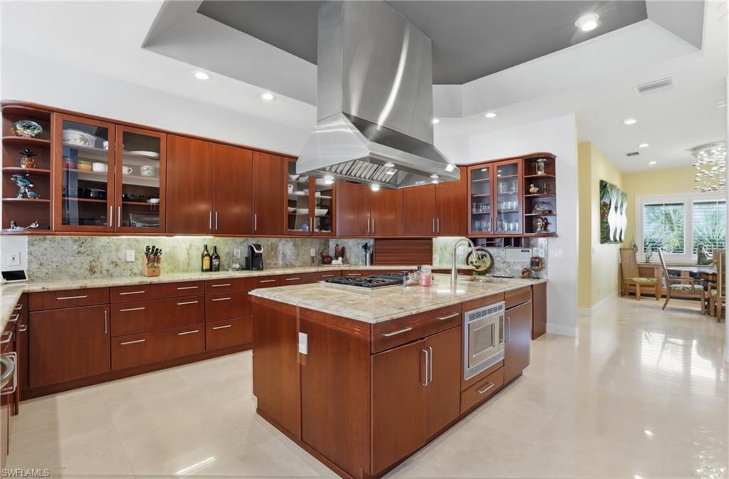 Kitchen with glass fronted cabinets, open shelves, light stone counters, island range hood, and stainless steel appliances