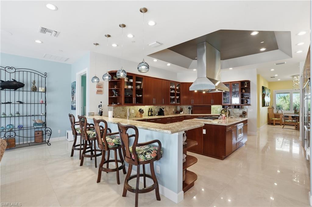 Kitchen featuring open shelves, glass fronted cabinets, a kitchen breakfast bar, a peninsula, and island exhaust hood