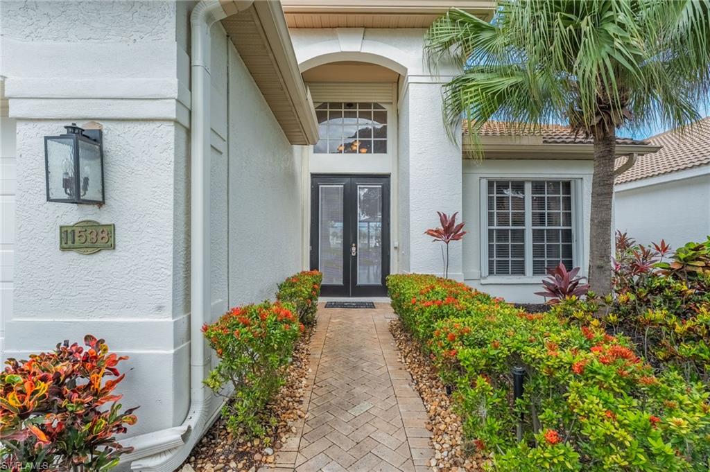 Stucco exterior featuring a paver walkway bordered by maintained shrubs and landscaping