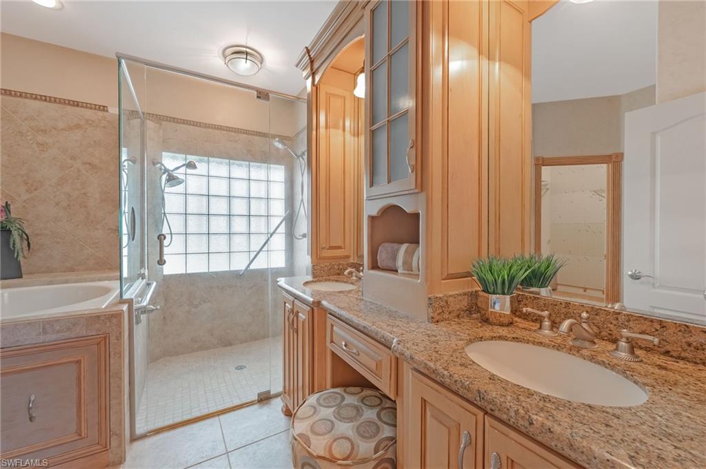 Master Bathroom featuring a dual vanity with granite countertops and undermount sinks, a built-in makeup area, extensive wood cabinetry, a glass-enclosed shower with multiple showerheads, and a built-in bathtub with tiled surround