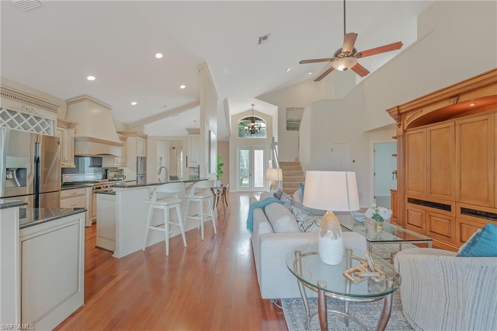 Open-concept living space featuring wood-finish flooring, a kitchen island with seating, stainless steel appliances, vaulted ceilings, and a built-in entertainment center