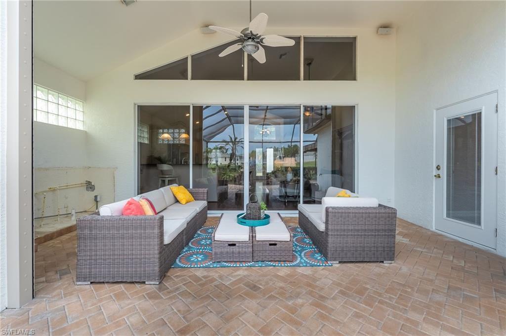 Spacious screened patio featuring herringbone-patterned brick pavers, a high vaulted ceiling with a ceiling fan, large glass sliding doors, and transom windows for abundant light