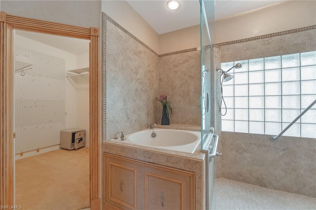 Bathroom featuring a built-in soaking tub, glass-enclosed shower with a glass block window, and extensive tile work