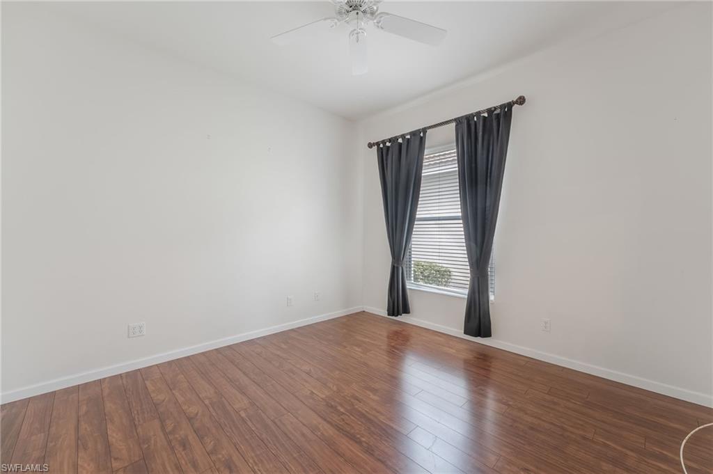Expansive second bedroom/study room featuring wood-finish flooring, white walls, and a white ceiling fan
