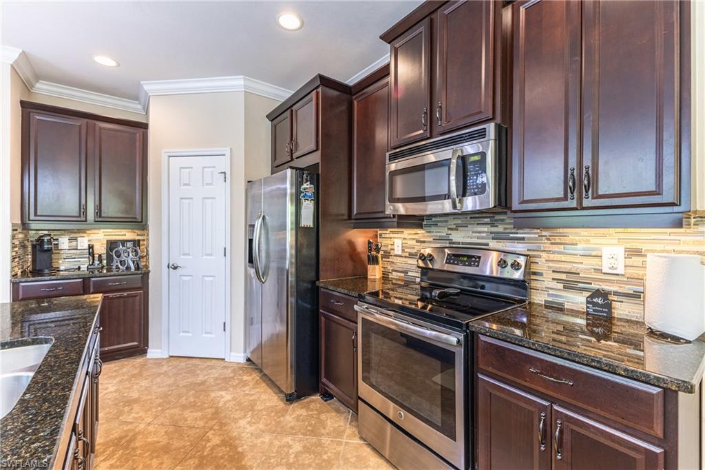 Kitchen with stainless steel appliances, dark stone counters, crown molding, dark wood finish cabinetry, and light tile patterned flooring