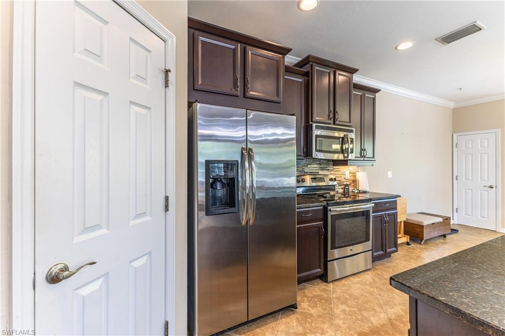 Kitchen featuring dark wood finish cabinetry, stainless steel appliances, ornamental molding, dark stone countertops, and light tile patterned floors