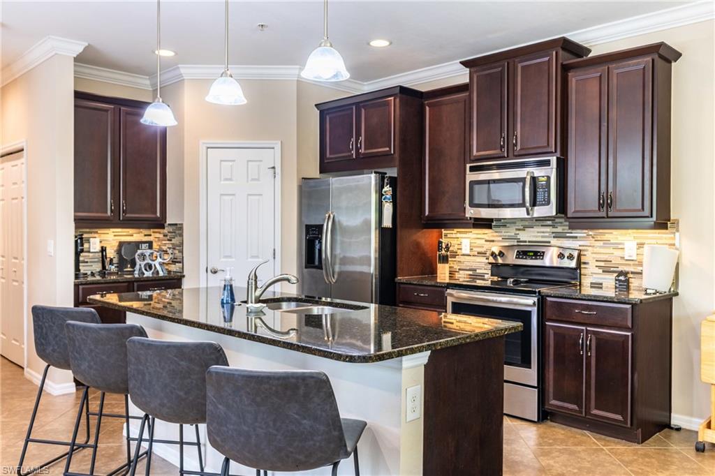 Kitchen with stainless steel appliances, dark stone countertops, a kitchen island with sink, a breakfast bar, and crown molding