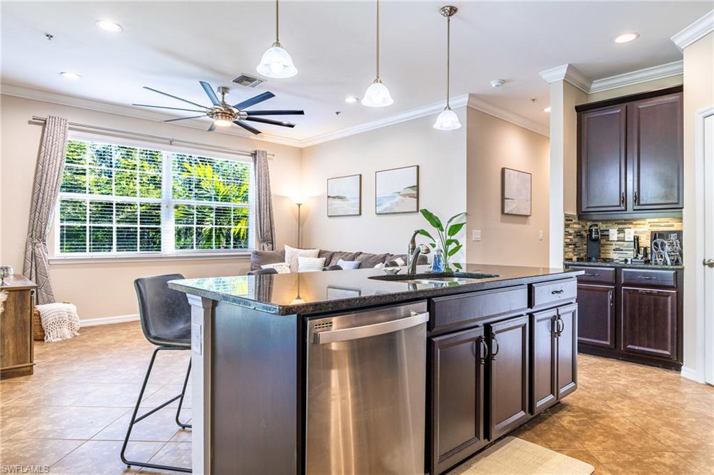 Kitchen featuring stainless steel dishwasher, a kitchen island with sink, a ceiling fan, hanging light fixtures, and ornamental molding