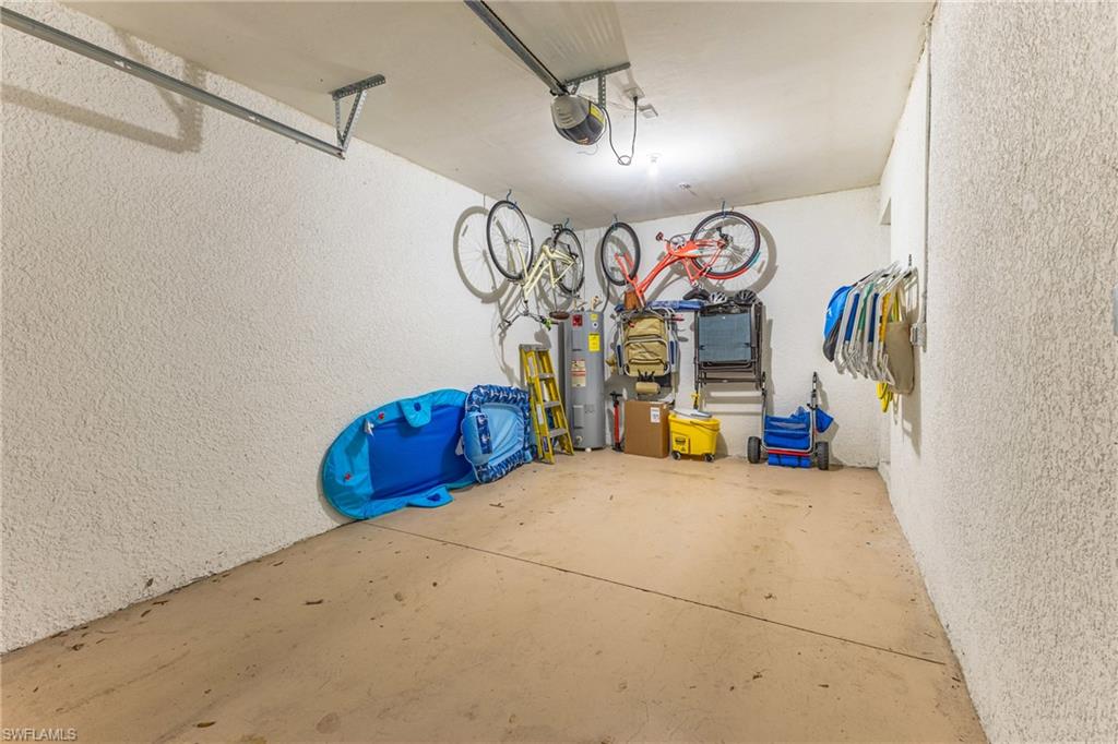 Garage with a textured wall, electric water heater, and a garage door opener