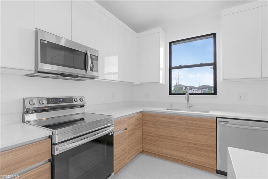Dual tone kitchen with stainless steel appliances, modern cabinets, light stone countertops, and two tone color scheme