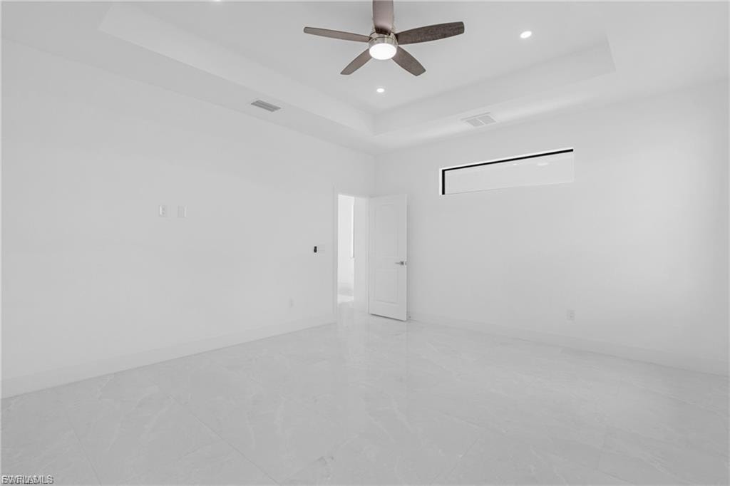 Empty room featuring a raised ceiling, ceiling fan, and recessed lighting