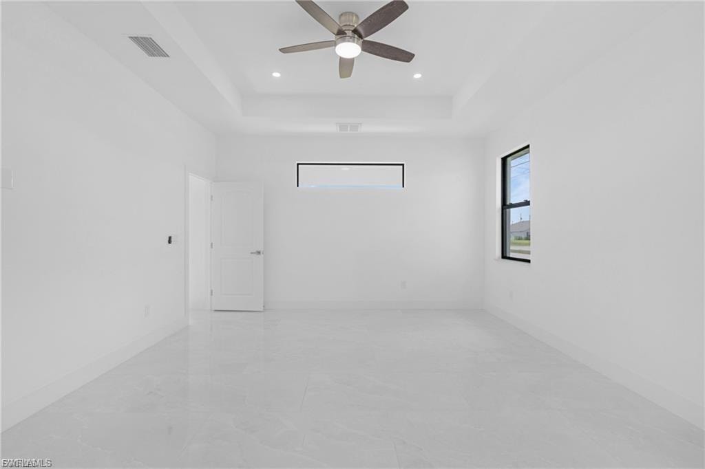 Empty room with a tray ceiling, ceiling fan, and recessed lighting