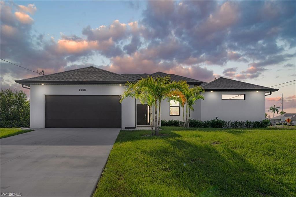 View of front of property with a garage, stucco siding, a yard, concrete driveway, and roof with shingles