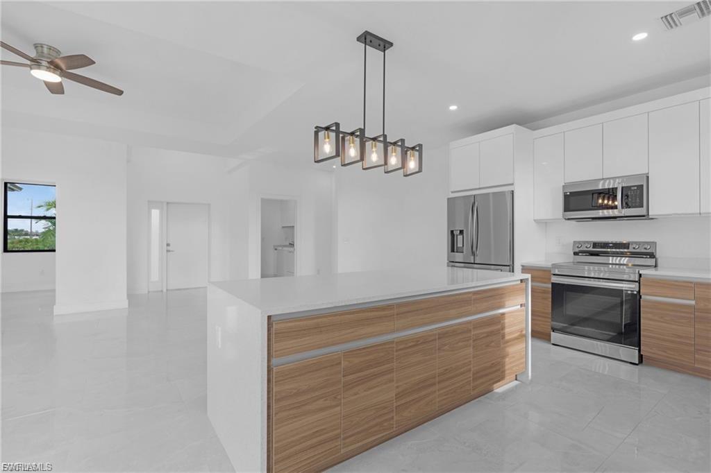 Two tone kitchen with stainless steel appliances, modern cabinets, a kitchen island, ceiling fan, and two tone cabinets