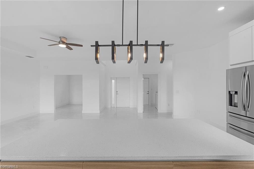 Kitchen featuring stainless steel refrigerator with ice dispenser, light stone countertops, pendant lighting, and a center island