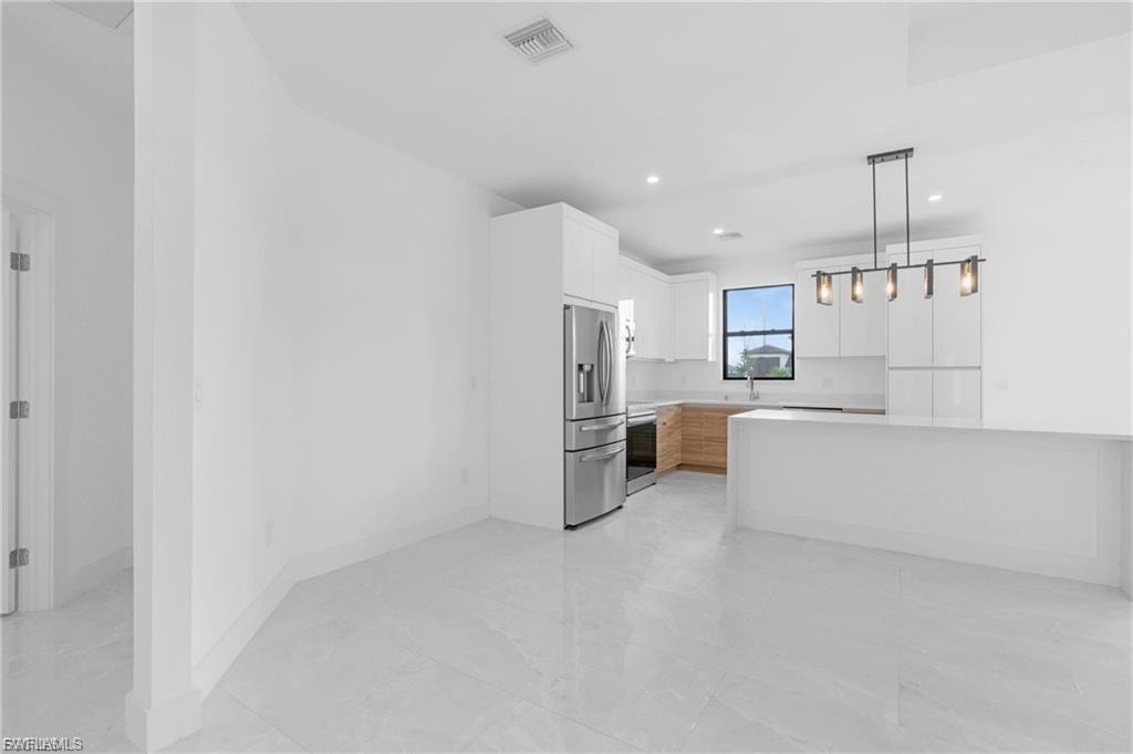 Kitchen featuring white cabinetry, stainless steel appliances, decorative light fixtures, and light stone countertops