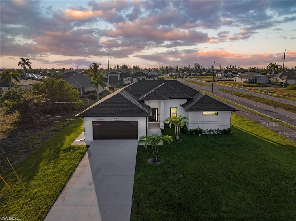 View of front of home with a yard, a shingled roof, stucco siding, and concrete driveway