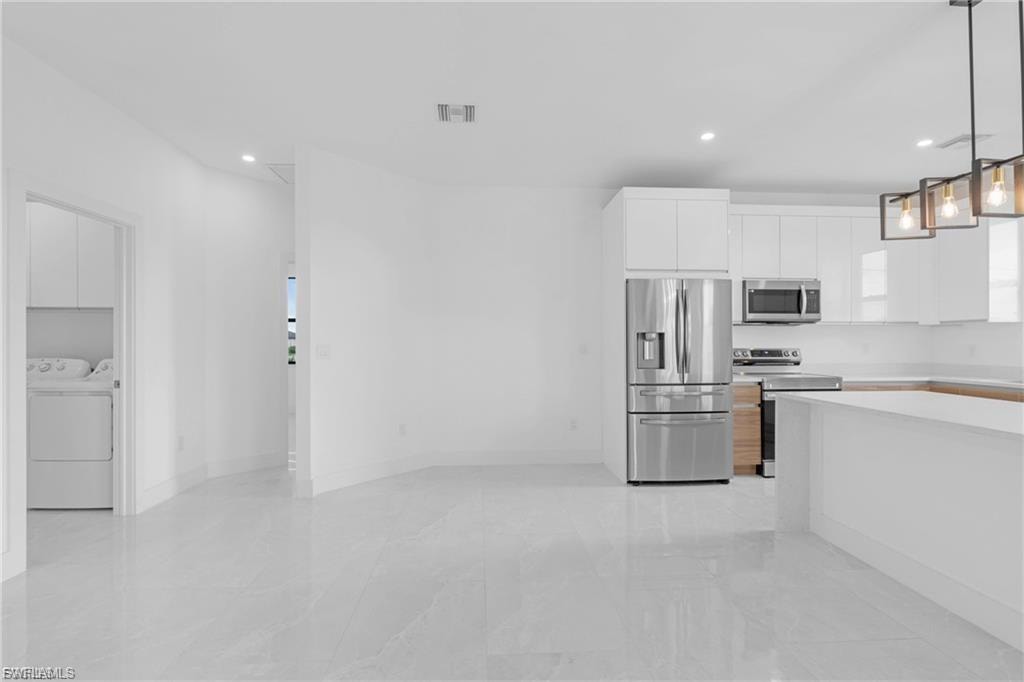 Two tone kitchen featuring stainless steel appliances, hanging light fixtures, dual tone cabinets, modern cabinets, and washing machine and dryer